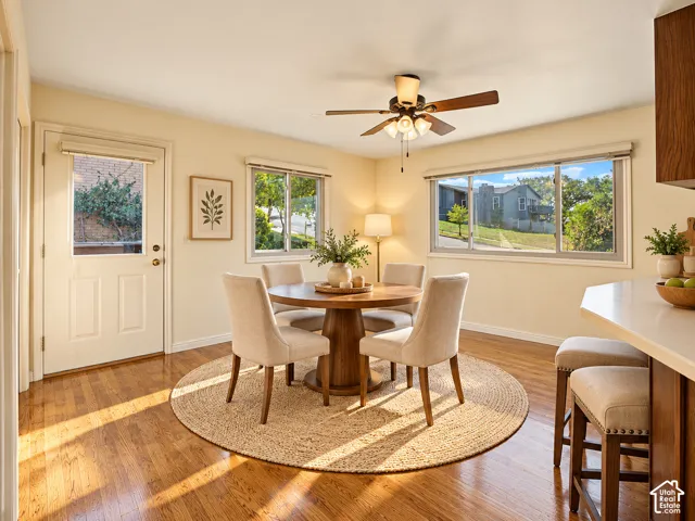 Wood-finish flooring, ceiling fan with integrated lighting, multiple windows, and a built-in breakfast bar with stools
