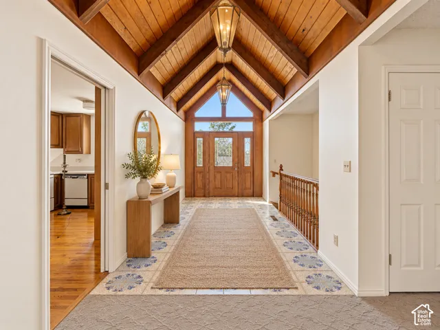 Vaulted wood-paneled ceiling with exposed beams, wood entry doors with transom window, tile flooring with decorative accents, and a wood staircase with balustrade