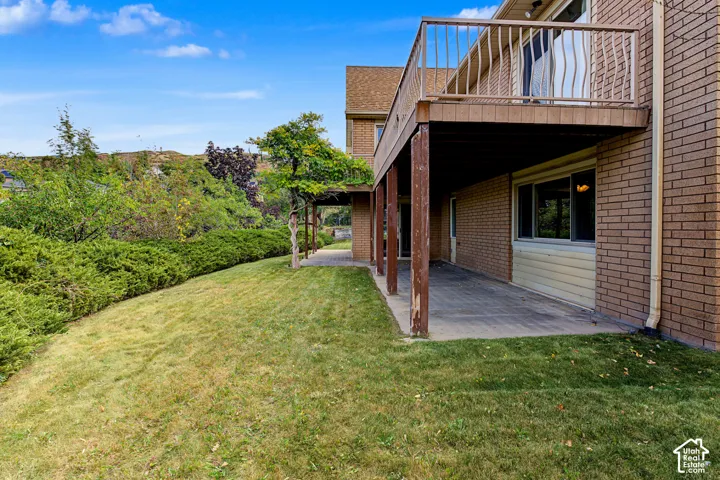 Brick exterior with a second-story balcony, covered patio, and sloped grassy area