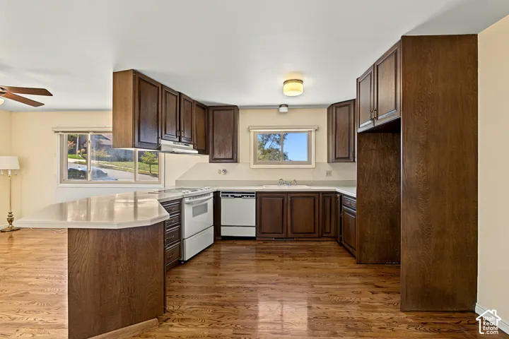 Kitchen featuring wood-finish flooring, extensive wood cabinetry, white countertops, and a built-in cooktop with oven
