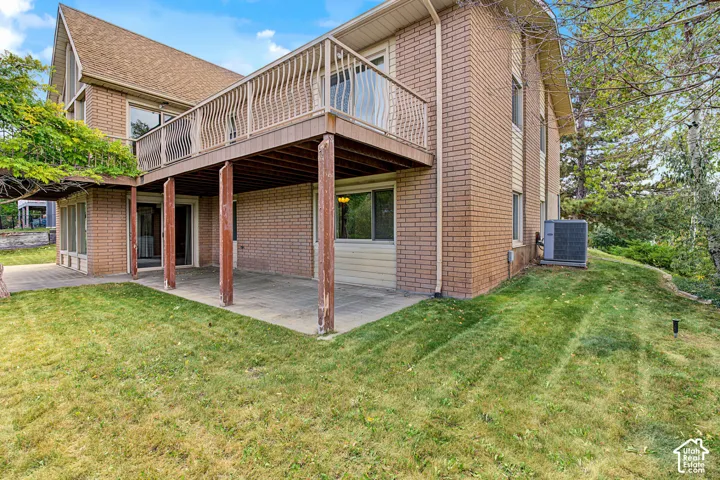 Brick exterior with a second-story balcony, a lower-level patio, and a sloped grassy area