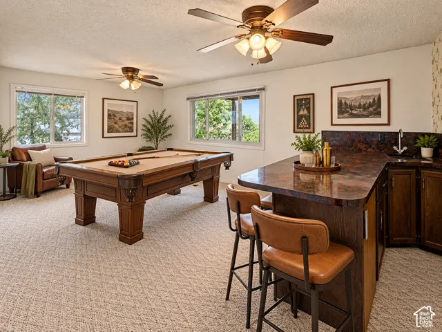 Flex space shown as game room Entertainment room featuring a built-in wet bar with a countertop and sink, patterned carpet flooring, and multiple windows