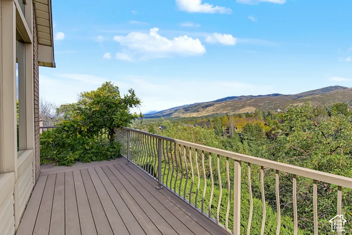 Expansive outdoor deck with composite decking, decorative metal railing, and an elevated position overlooking a mountainous landscape with abundant trees