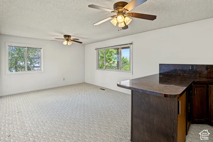 Open-concept room featuring a built-in counter with a dark stone-finish surface, recessed paneled cabinetry, and two ceiling fans with integrated lighting