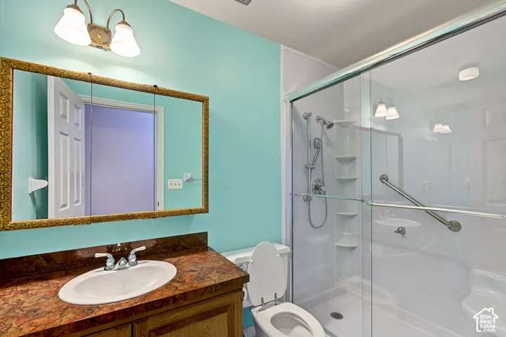Bathroom featuring a wood-finish vanity with an oval sink, a framed mirror, a two-light vanity fixture, and a walk-in shower with a glass enclosure and grab bars