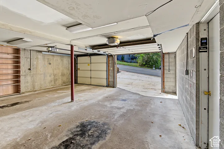 Concrete block walls, concrete flooring, overhead lighting, built-in shelving, and an automatic garage door opener