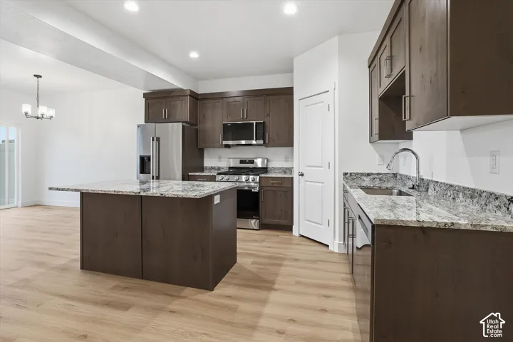 Kitchen with wood-finish flooring, dark wood cabinetry, stainless steel appliances, speckled stone countertops, and a central island