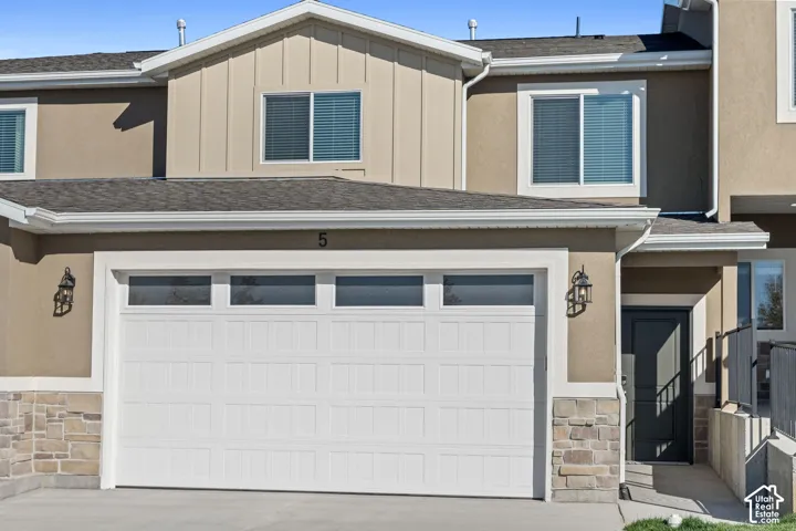 Exterior featuring a white paneled garage door with upper lites, stone veneer accents, and a dark entry door