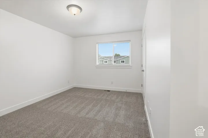 Neutral tone wall paint, carpet flooring, a single window, and a flush-mount ceiling light fixture