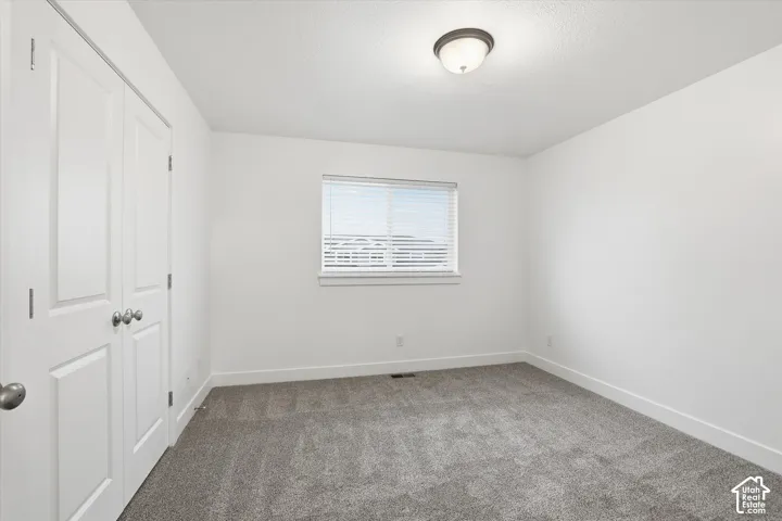 Carpeted room with white walls, a single window with blinds, and a flush-mount ceiling light