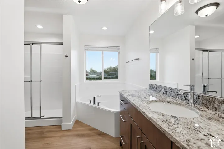 Spacious bathroom featuring a built-in soaking tub, separate glass-enclosed shower with subway tile, wood-finish flooring, and a vanity with a stone countertop