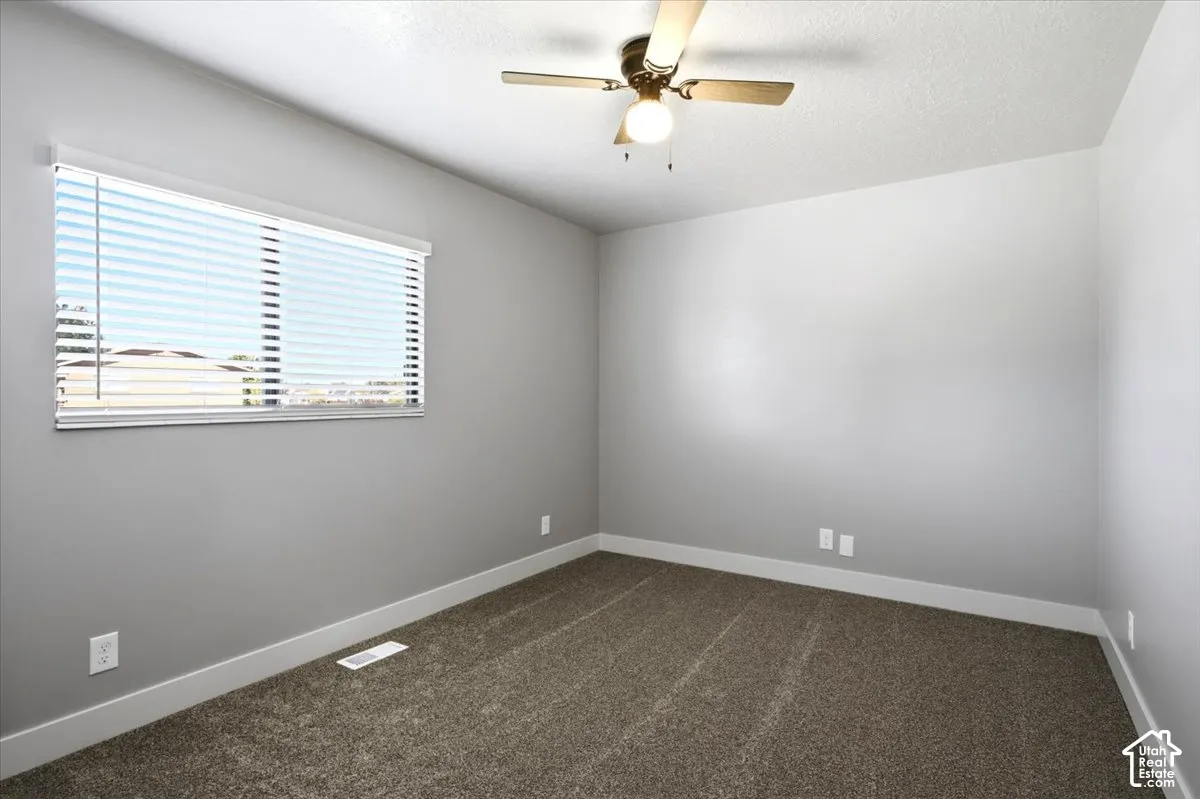Neutral gray walls with white trim, brown carpet, window with horizontal blinds, and a brass-finish ceiling fan with light fixture