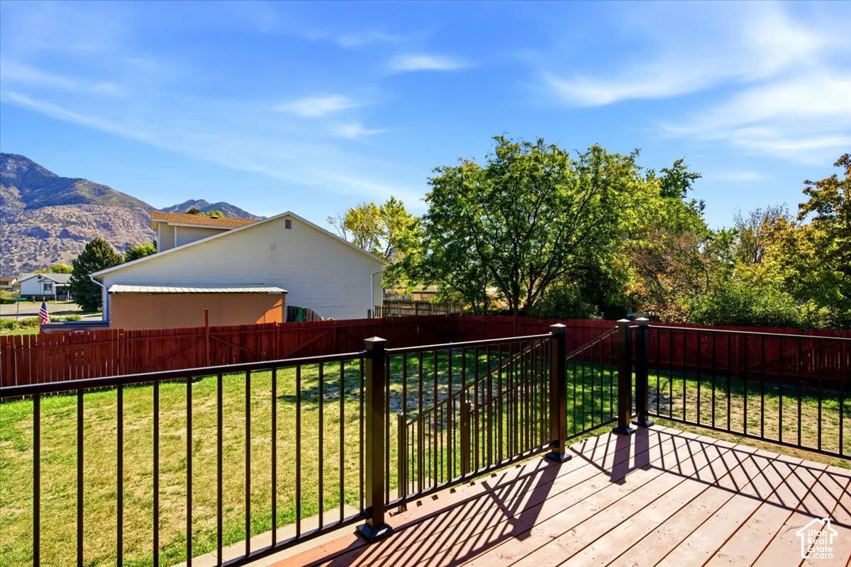 Expansive wood-finish deck with black metal railings, overlooking a large grassy yard with a solid privacy fence and mature trees