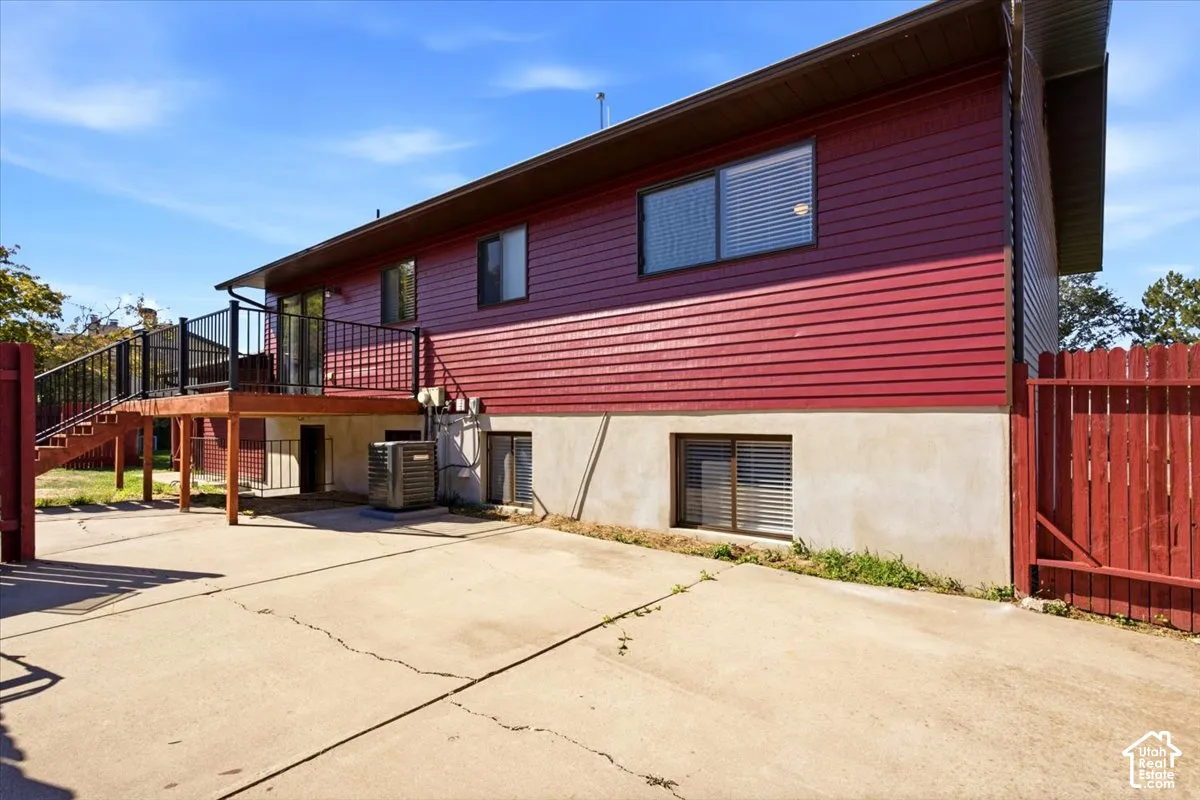 Exterior featuring red horizontal siding, a raised wood deck with black railings, concrete paving, and a red wood fence