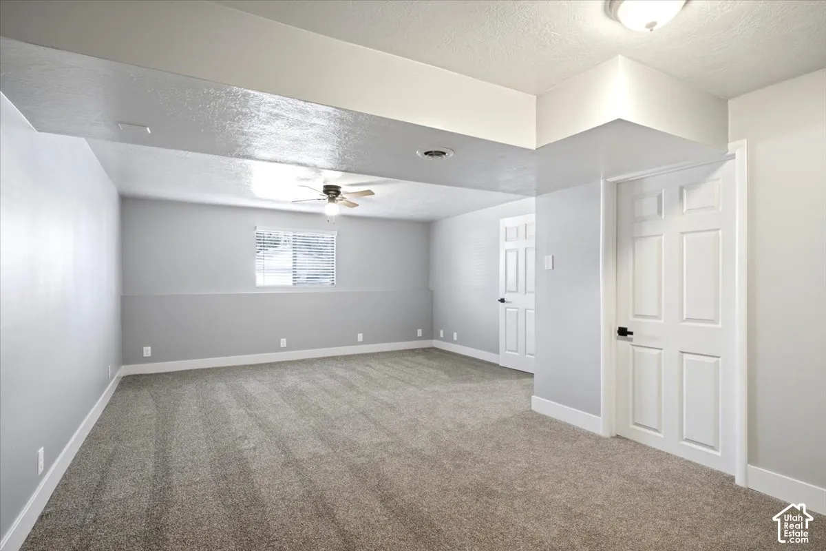 Spacious room with plush carpeting, neutral two-tone wall paint, and a ceiling fan with integrated lighting