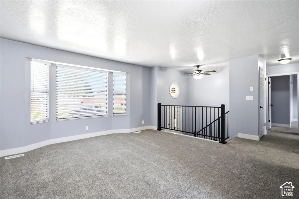 Spacious room featuring a bay window, plush grey carpet, and a black wrought iron railing