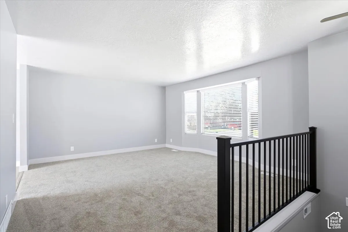 Expansive room with neutral carpeting, light gray wall tones, and multiple windows featuring blinds
