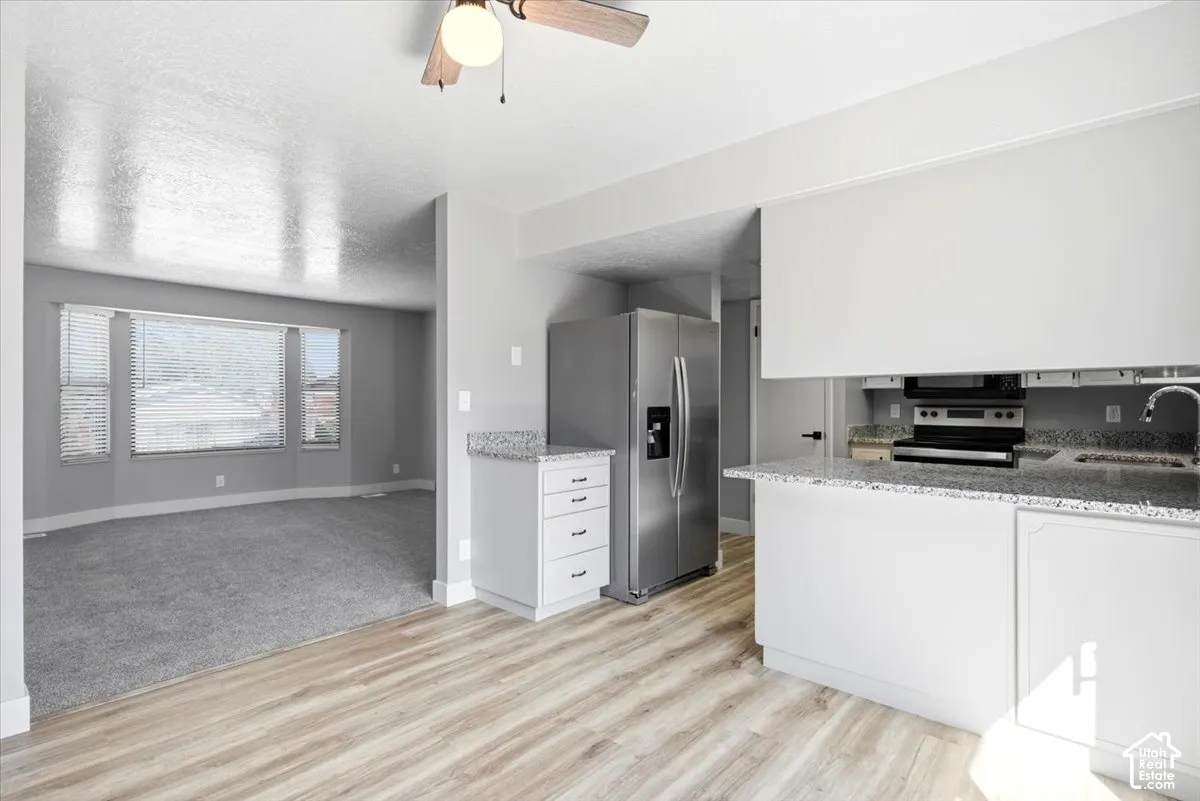 Kitchen featuring wood-finish flooring, white cabinetry, granite countertops, and stainless steel appliances