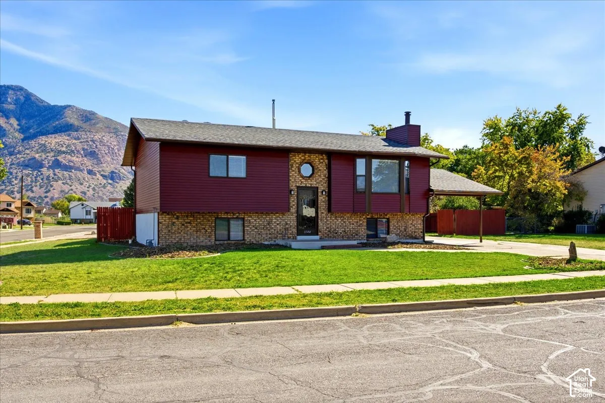 Split-level residence featuring brick and siding exterior, a front yard with mature landscaping, and a covered carport