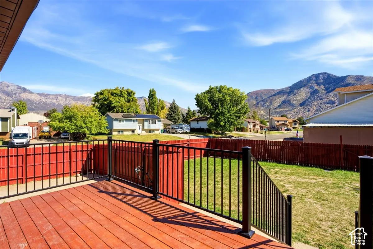 Wood-finish deck with black metal railing, overlooking a fenced yard and distant mountains