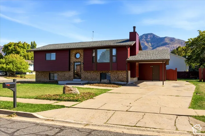 Red siding exterior with stone accent, asphalt shingle roof, attached carport, and a prominent mountain backdrop