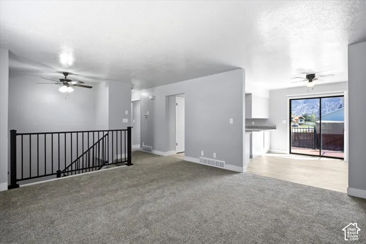 Open-concept living space featuring carpeted flooring, a ceiling fan, and a black metal staircase railing