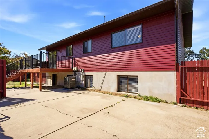Exterior featuring red horizontal siding, a raised wood deck with black railings, concrete paving, and a red wood fence