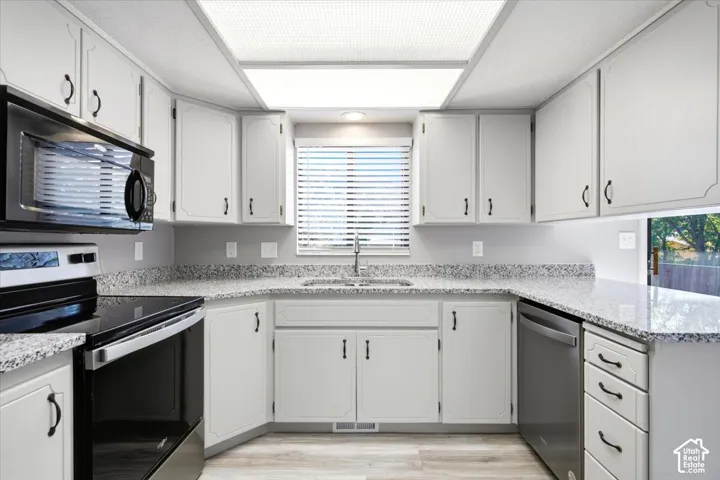 Kitchen with light cabinetry, black appliances, speckled countertops, and wood-finish flooring