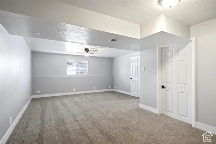 Spacious room with plush carpeting, neutral two-tone wall paint, and a ceiling fan with integrated lighting