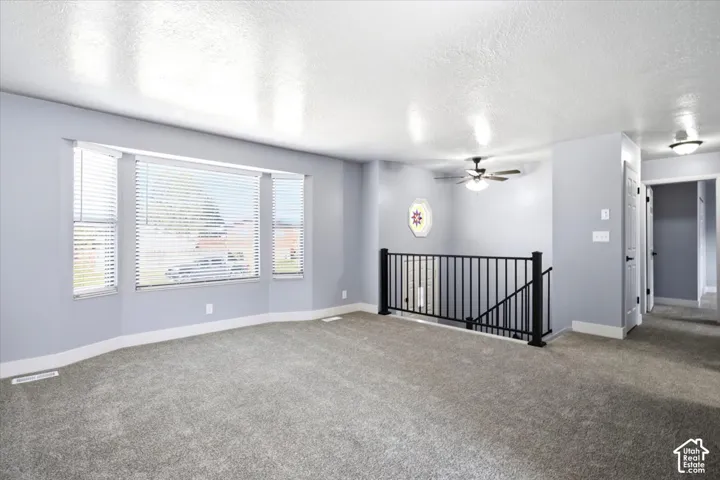 Spacious room featuring a bay window, plush grey carpet, and a black wrought iron railing