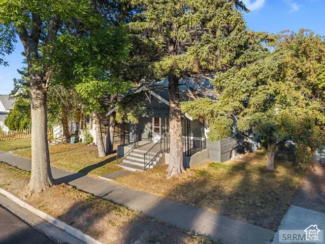 Exterior featuring a covered porch, concrete steps with black metal railings, and mature trees