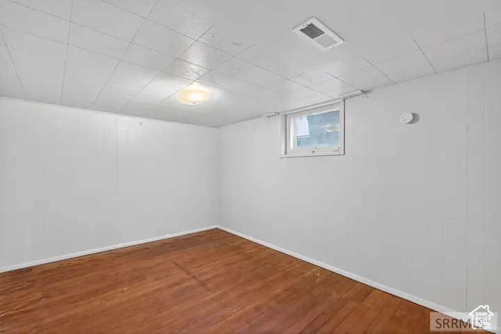 Wood-finish flooring with white paneled walls, a drop ceiling, and a flush-mount light fixture