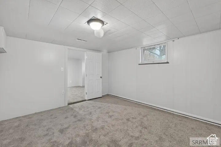 Carpeted room featuring a drop ceiling, white paneled walls, and a window