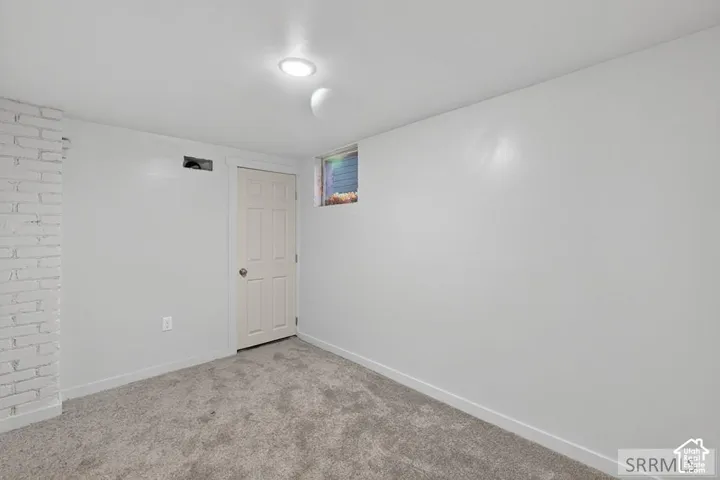 White painted brick accent wall, white painted walls, textured gray carpet, single recessed ceiling light, and a white paneled door