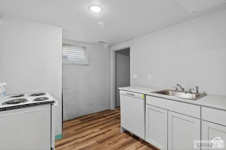 White cabinetry, wood-finish flooring, stainless steel sink, recessed lighting, and white appliances