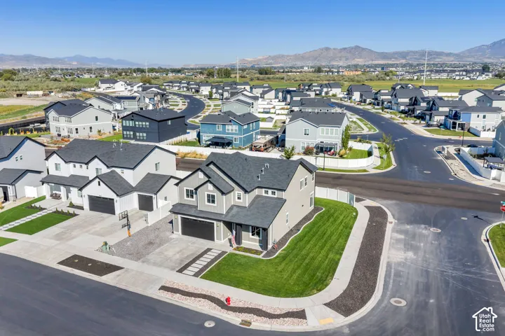 Corner lot residence featuring a two-car garage, manicured lawn, and a light-toned exterior with dark trim