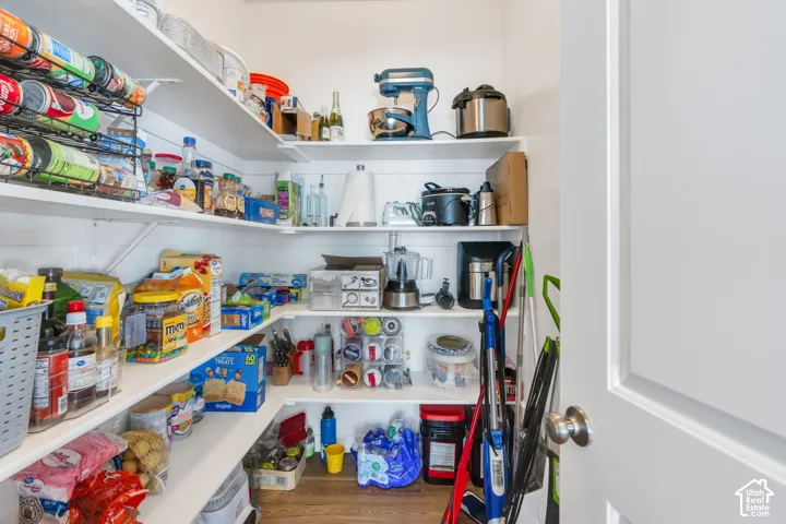 Walk-in pantry featuring white shelving, wood-finish flooring, and a white panel door