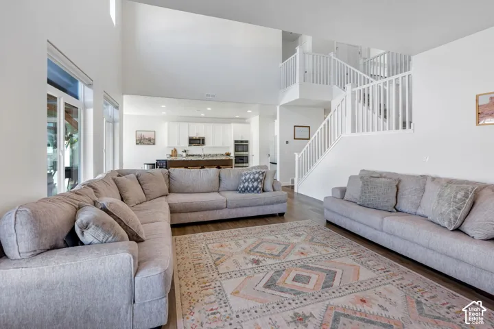 Open-concept living area featuring a two-story ceiling, wood-finish flooring, and a white staircase with balusters