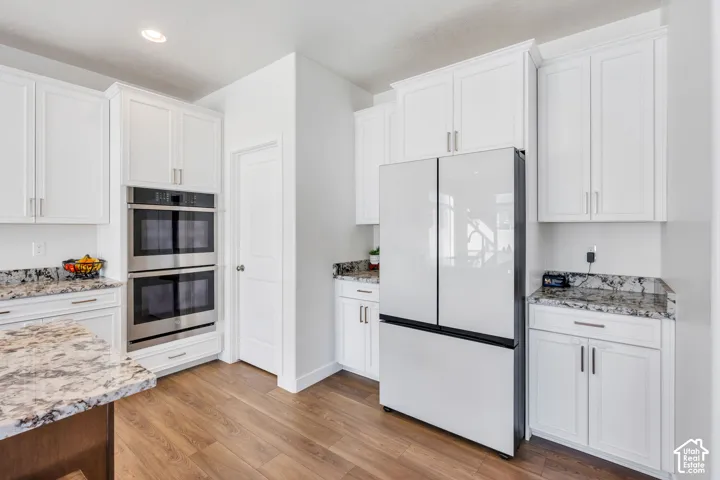 White cabinetry, stainless steel double wall oven, wood-finish flooring, recessed lighting, and light-toned countertops