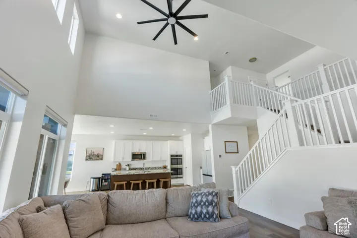 Vaulted ceiling with a black ceiling fan, large windows, white kitchen cabinetry, multi-level staircase with white railings, and wood-finish flooring