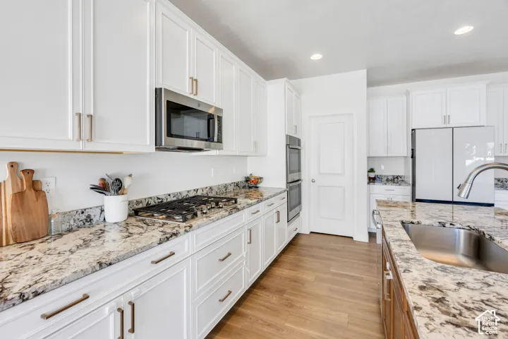White cabinetry with brushed nickel hardware, stainless steel appliances, granite countertops, wood-finish flooring, and a stainless steel sink with a high-arc faucet