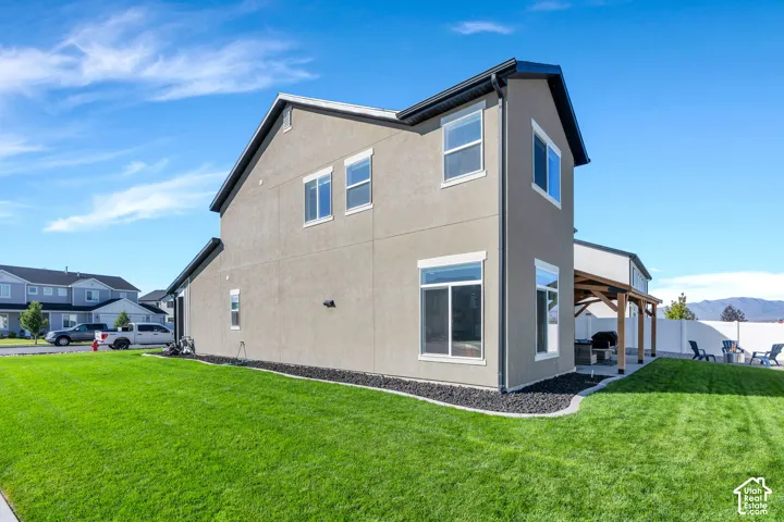 Stucco exterior with multiple windows, a wood pergola, and a grassy lawn with dark rock landscaping