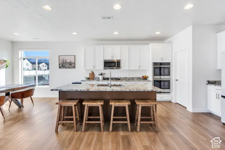 Kitchen featuring a large island with stone countertop, white upper and lower cabinetry, and stainless steel double ovens