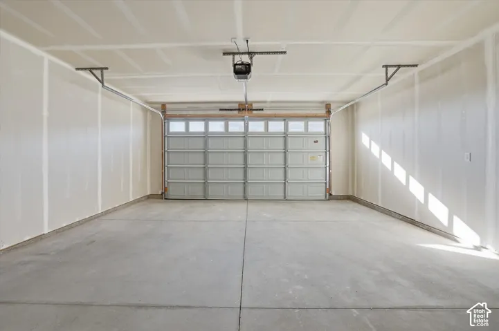 Concrete flooring, automatic garage door opener, overhead lighting, finished walls, and a sectional garage door with window inserts