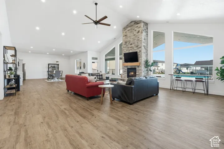 Spacious open-concept living area featuring wood-finish flooring, a stone-clad fireplace, and large windows