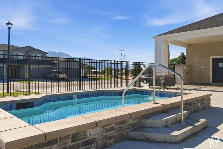 Outdoor spa with integrated steps, stone-finish surround, and metal handrail, adjacent to a covered patio