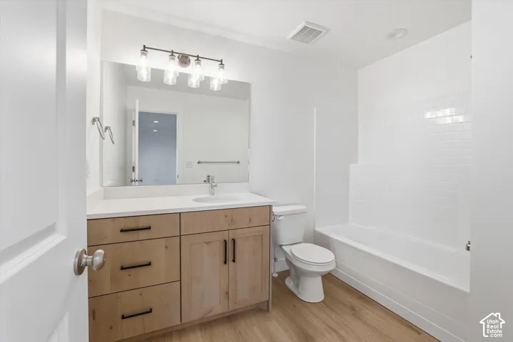 Wood-finish flooring, light wood vanity with dark hardware, undermount sink, white countertop, and a white subway-tiled tub with shower
