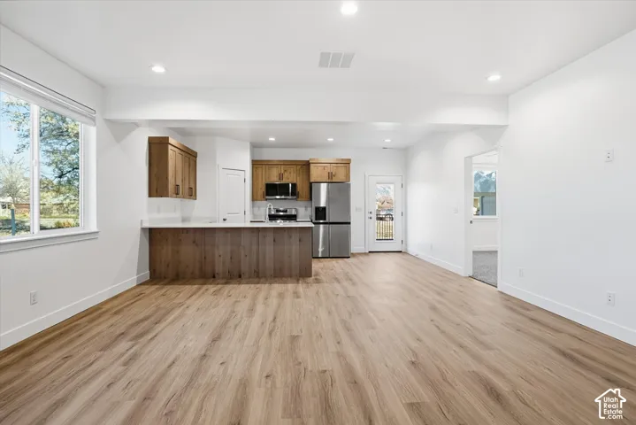 Open-concept living space featuring wood-finish flooring, recessed lighting, and a kitchen with wood cabinetry, stainless steel appliances, and a breakfast bar