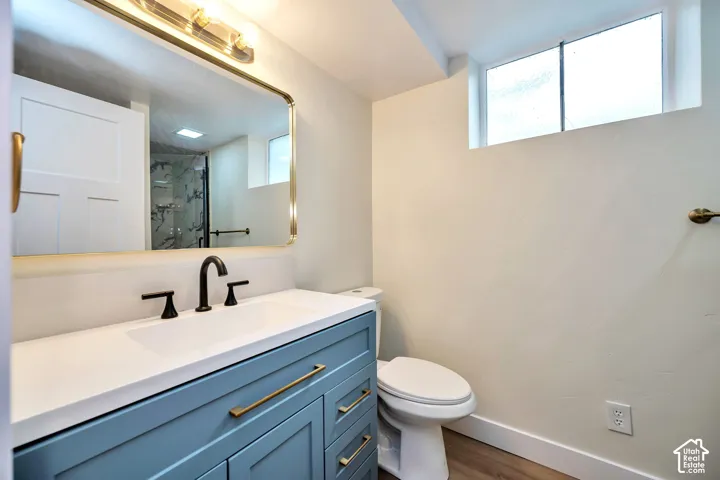 Modern bathroom featuring a blue vanity with dual brass hardware pulls, white quartz countertop, matte black faucet, and an illuminated framed mirror