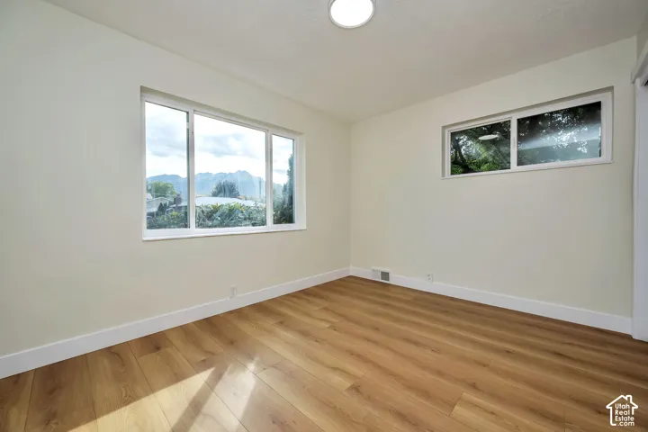Bright, light-filled bedroom showcasing hardwood flooring, recessed ceiling lighting, and expansive windows framing scenic outdoor vistas